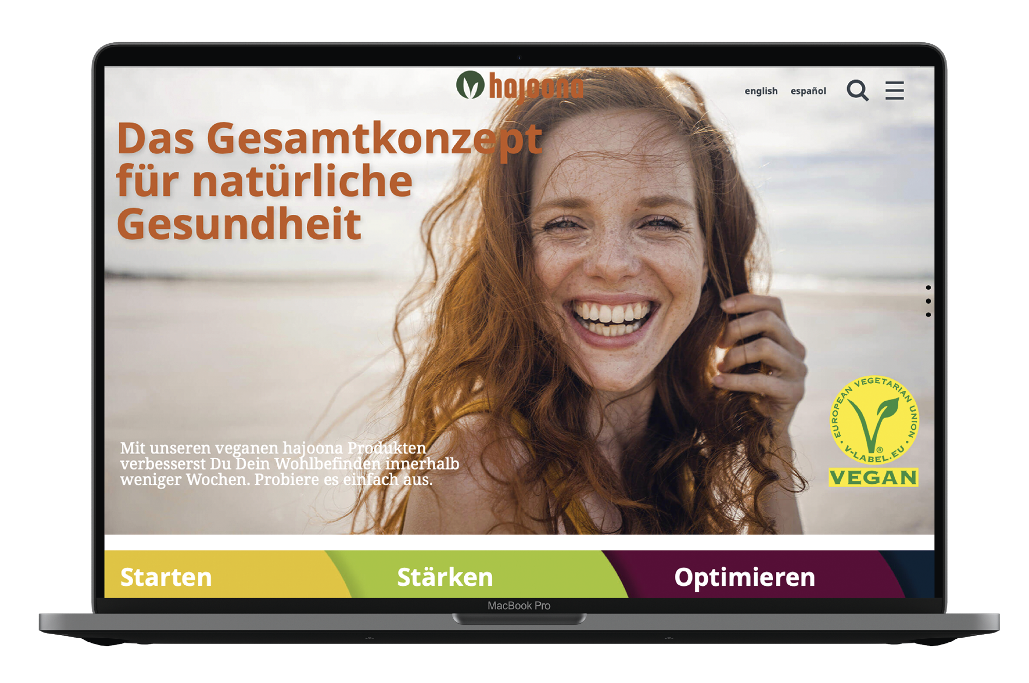 Laptop mit geöffneter Website von hajooona, auf der eine lächelnde Frau und der Schriftzug „Das Gesamtkonzept für natürliche Gesundheit“ zu sehen sind, daneben das gelbe Vegan-Siegel.