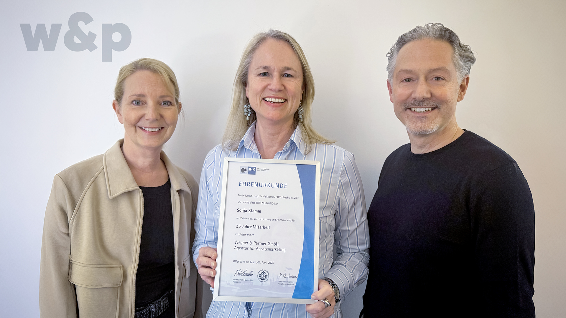 Drei Personen stehen zusammen und halten eine Urkunde zum 25-jährigen Jubiläum.